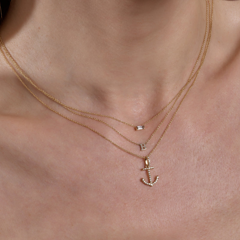 model wearing layered gold necklaces featuring an initial, diamond solitare, and anchor charm.