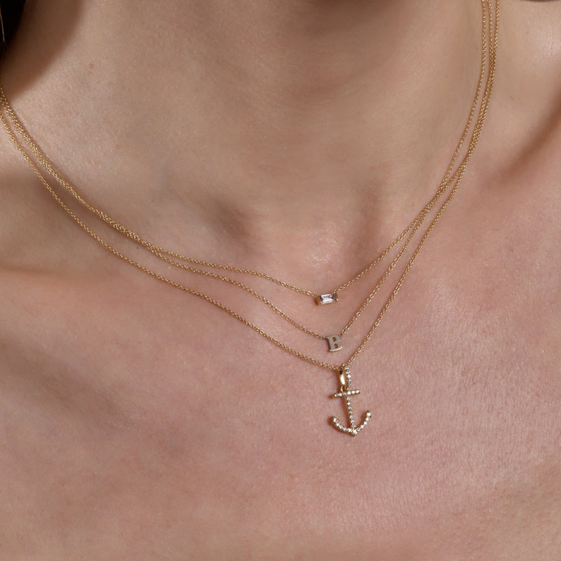 Layered gold necklaces featuring an initial, diamond solitaire pendant, and anchor charm by Phoenix Roze