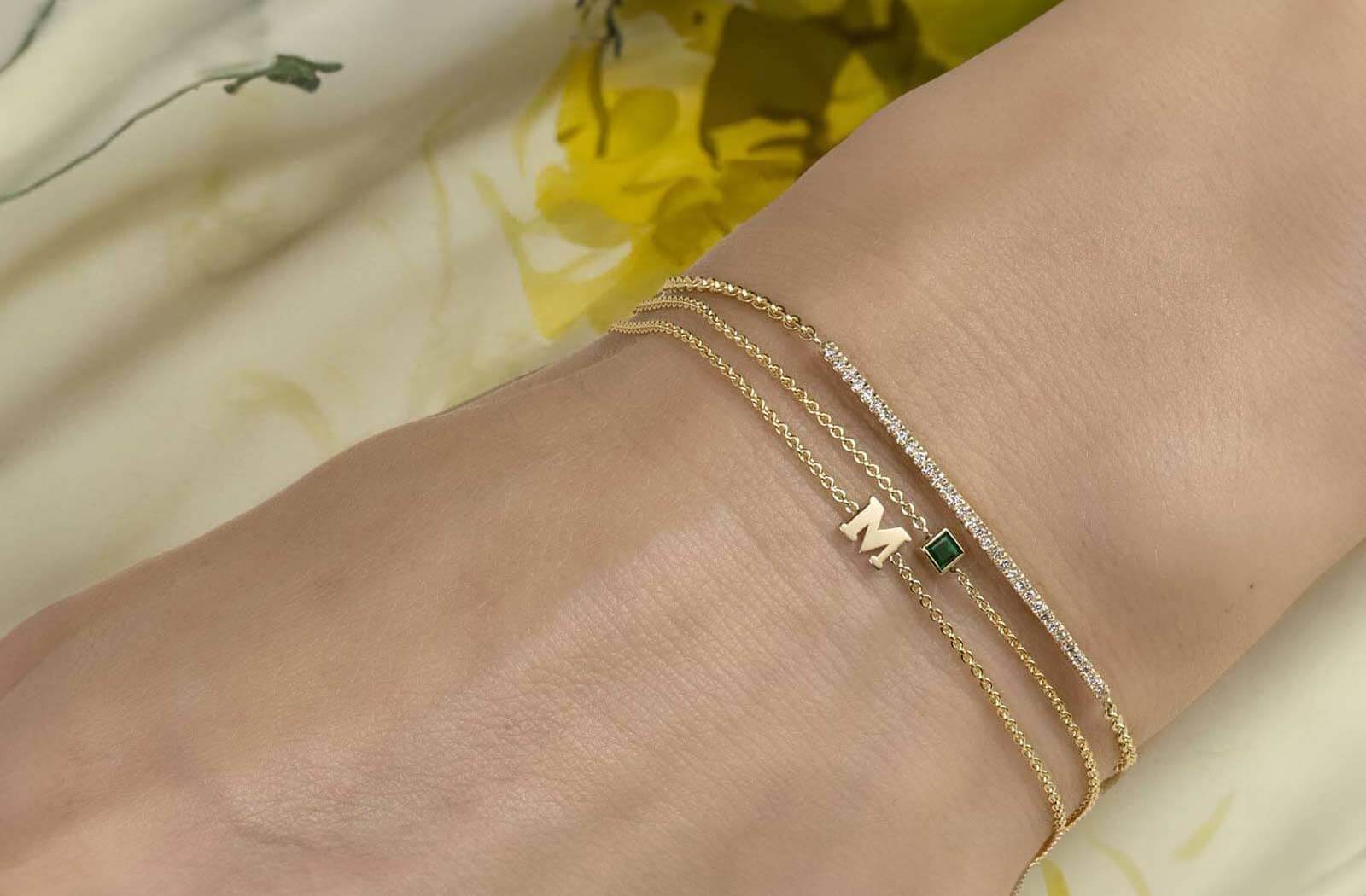 Model wearing bracelets featured in our Mother's Day Gift Guide. Including, our gold initial, square gemstone, and diamond bar bracelets.