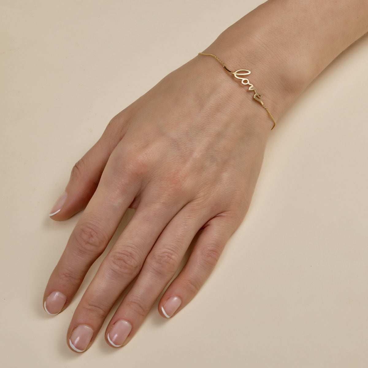 Dainty cursive gold “love” bracelet on a woman’s wrist, elegant script jewelry and romantic gift idea