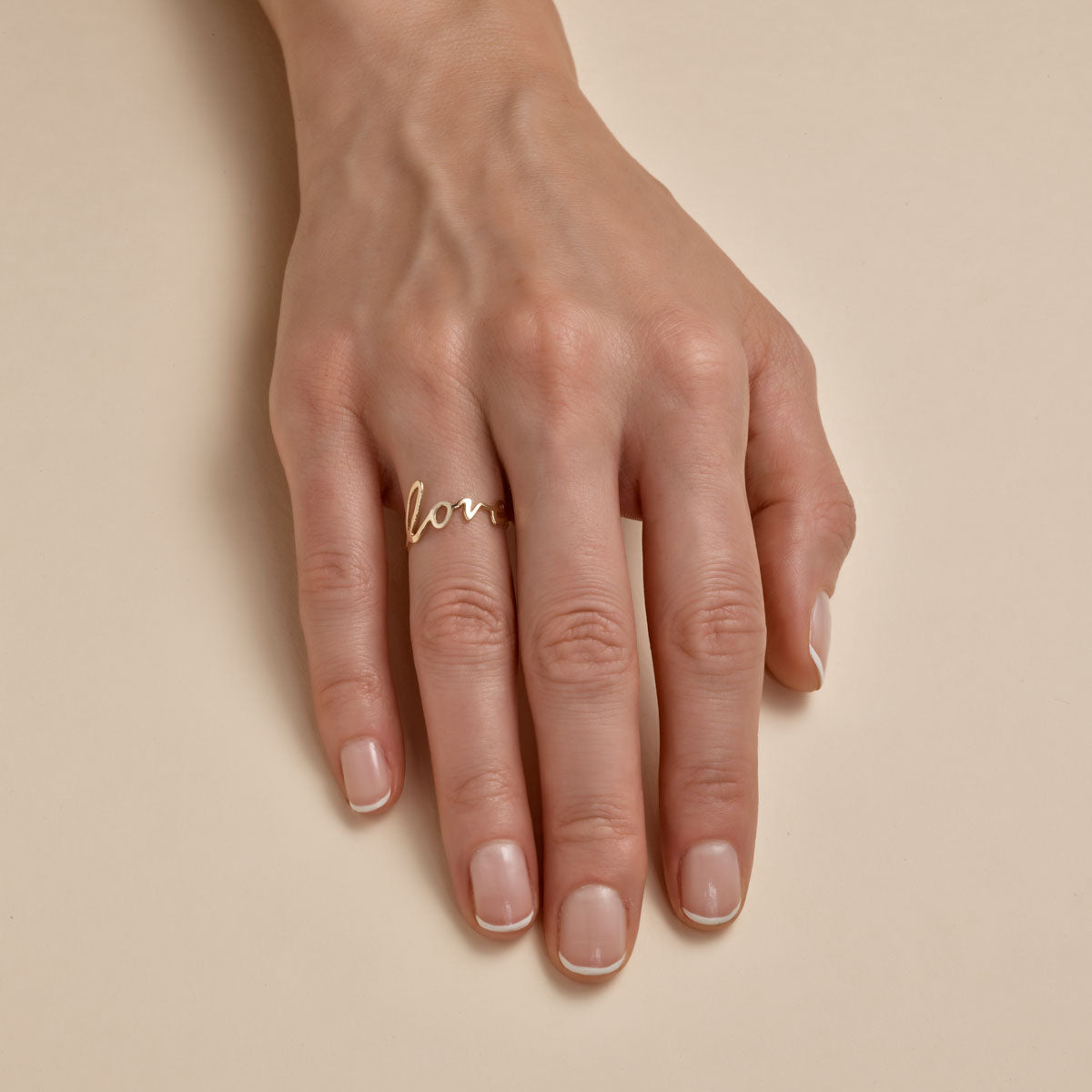 Cursive love ring on a woman’s finger, delicate script design—romantic minimalist jewelry by Phoenix Roze.