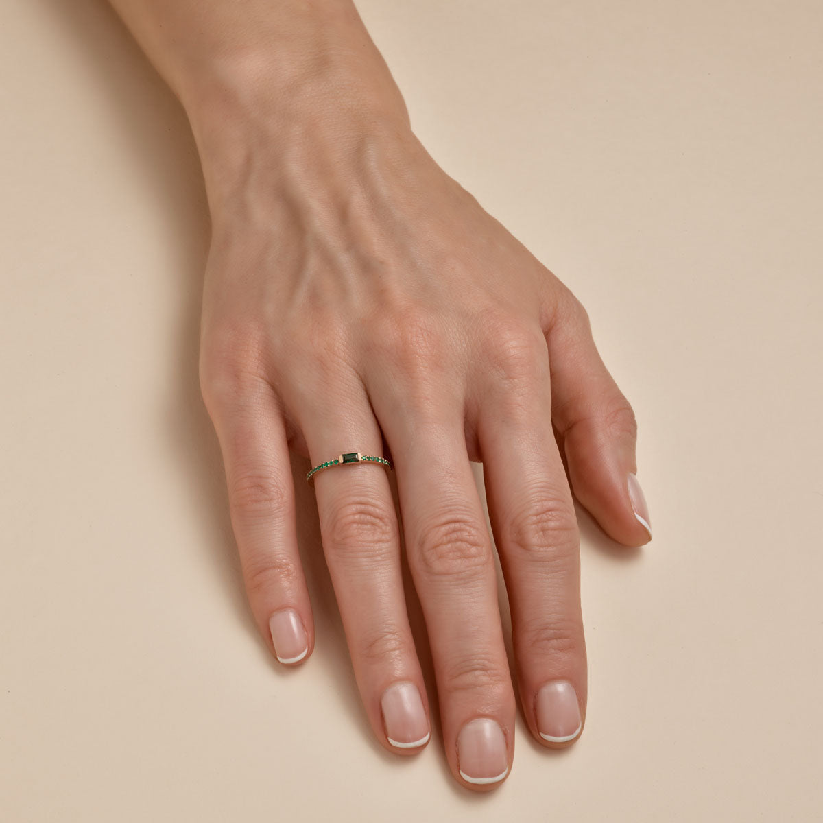 Emerald baguette ring on woman's finger, slim gold band with vivid green gemstone, elegant fine jewelry by Phoenix Roze