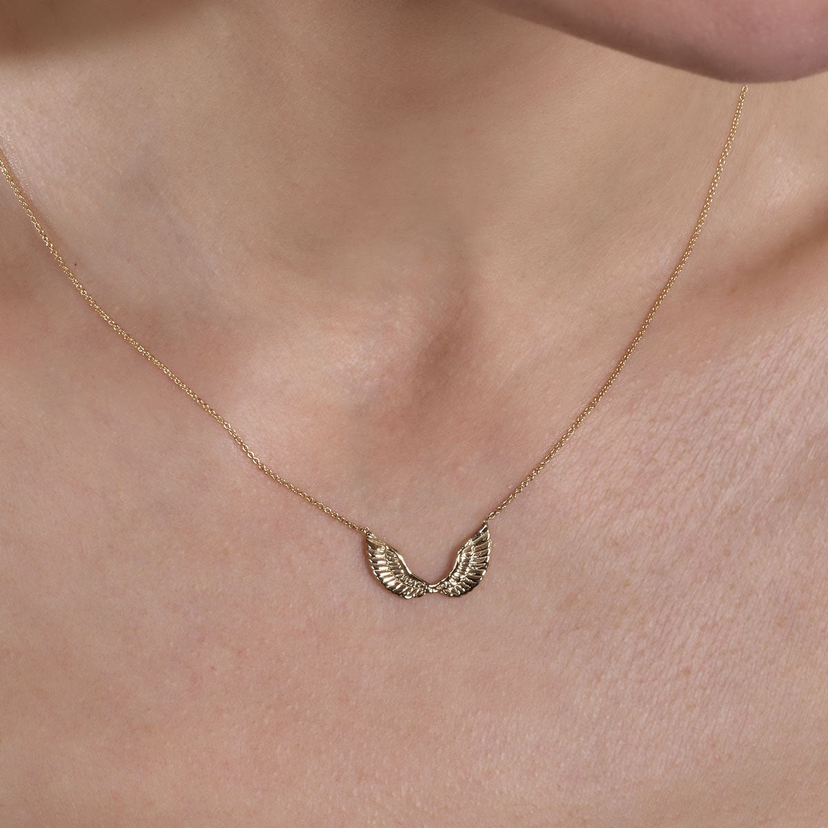 Gold angel wings pendant necklace on a woman's neck, delicate and elegant jewelry