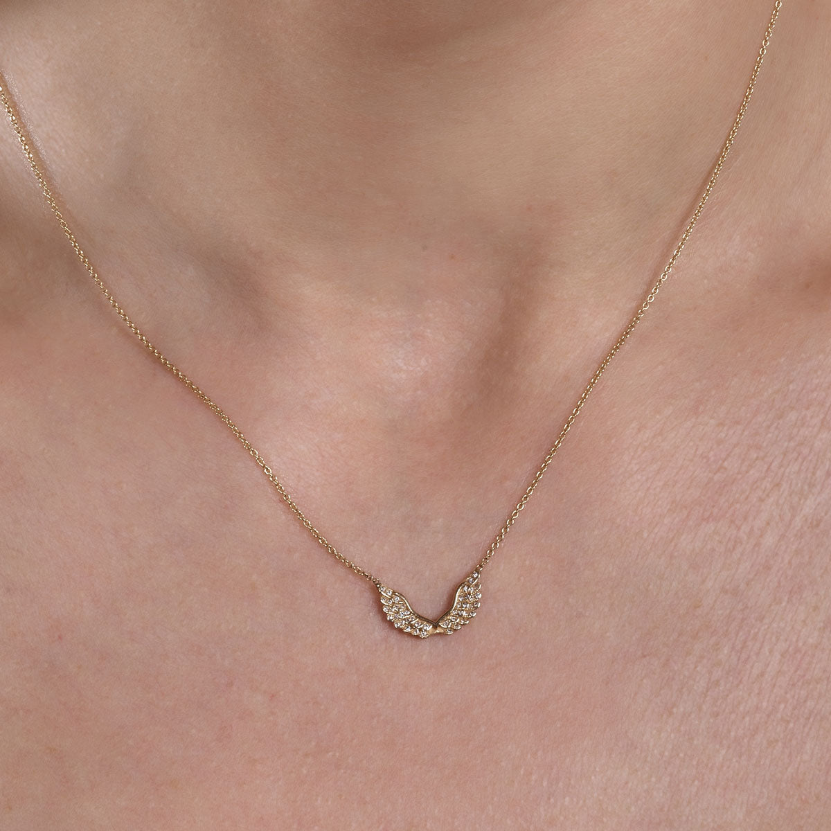 Phoenix Roze gold diamond angel wings necklace on neck, delicate pendant sparkles on model's neckline