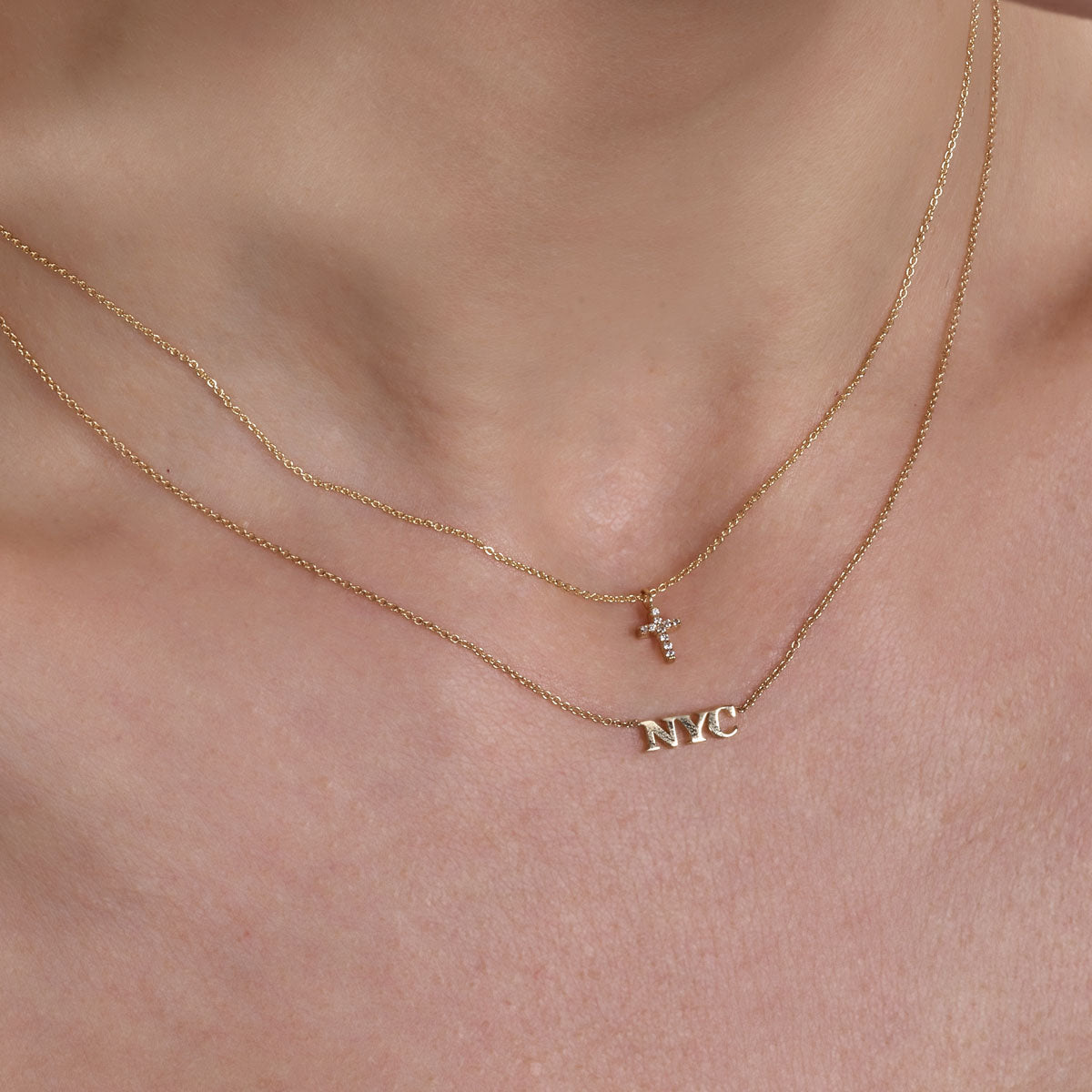 Gold diamond cross necklace layered with gold NYC necklace on neck - Phoenix Roze fine jewelry