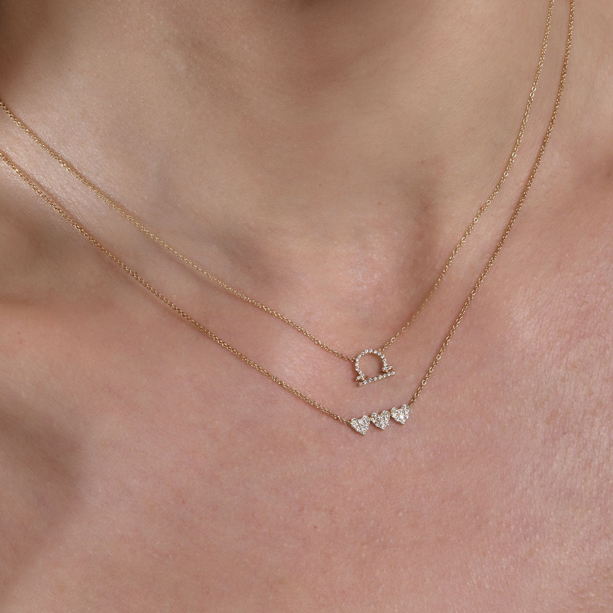 Gold diamond Libra necklace and gold diamond triple heart necklace layered on neck, delicate sparkle.