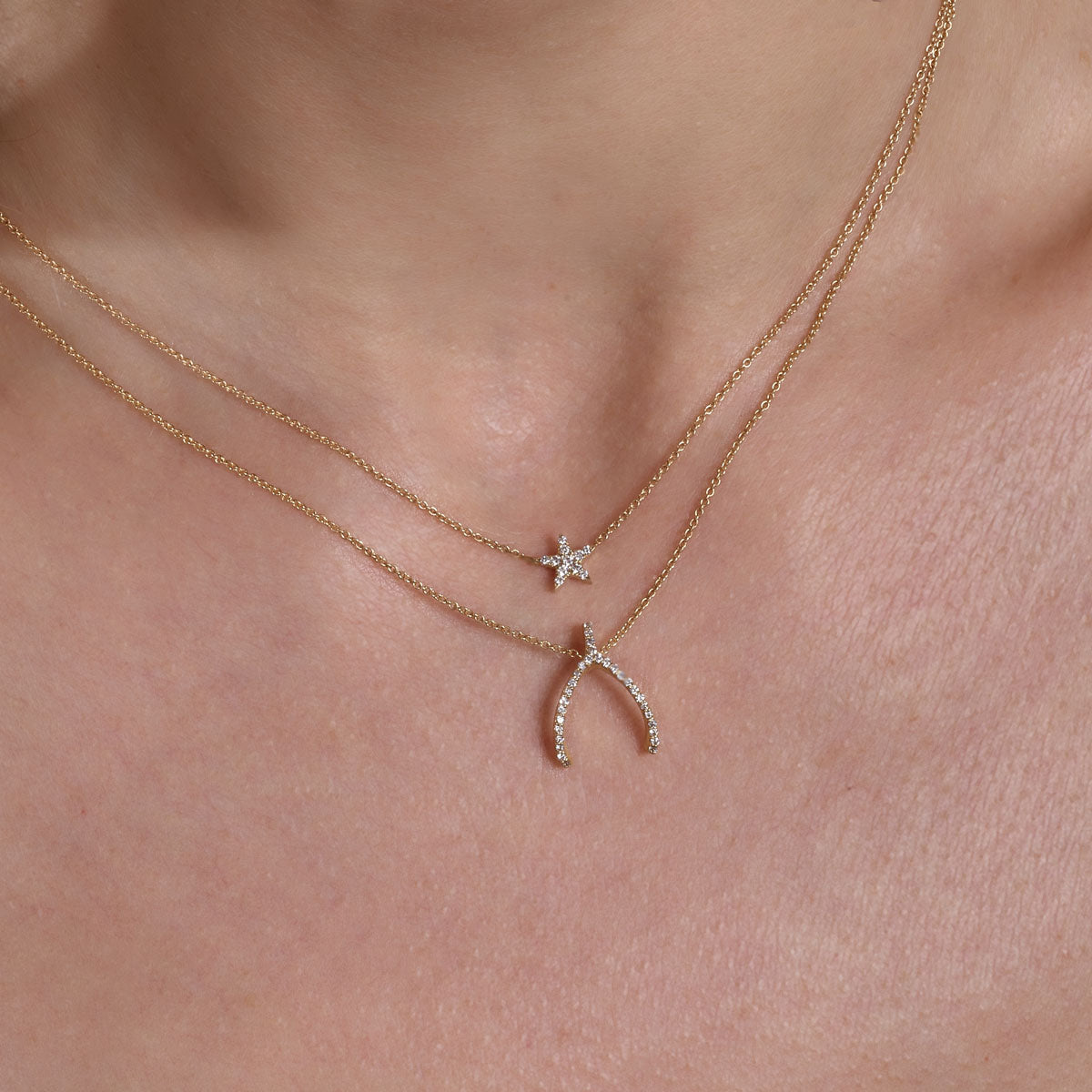 Layered gold diamond star necklace and gold diamond wishbone necklace on model’s neck - Phoenix Roze