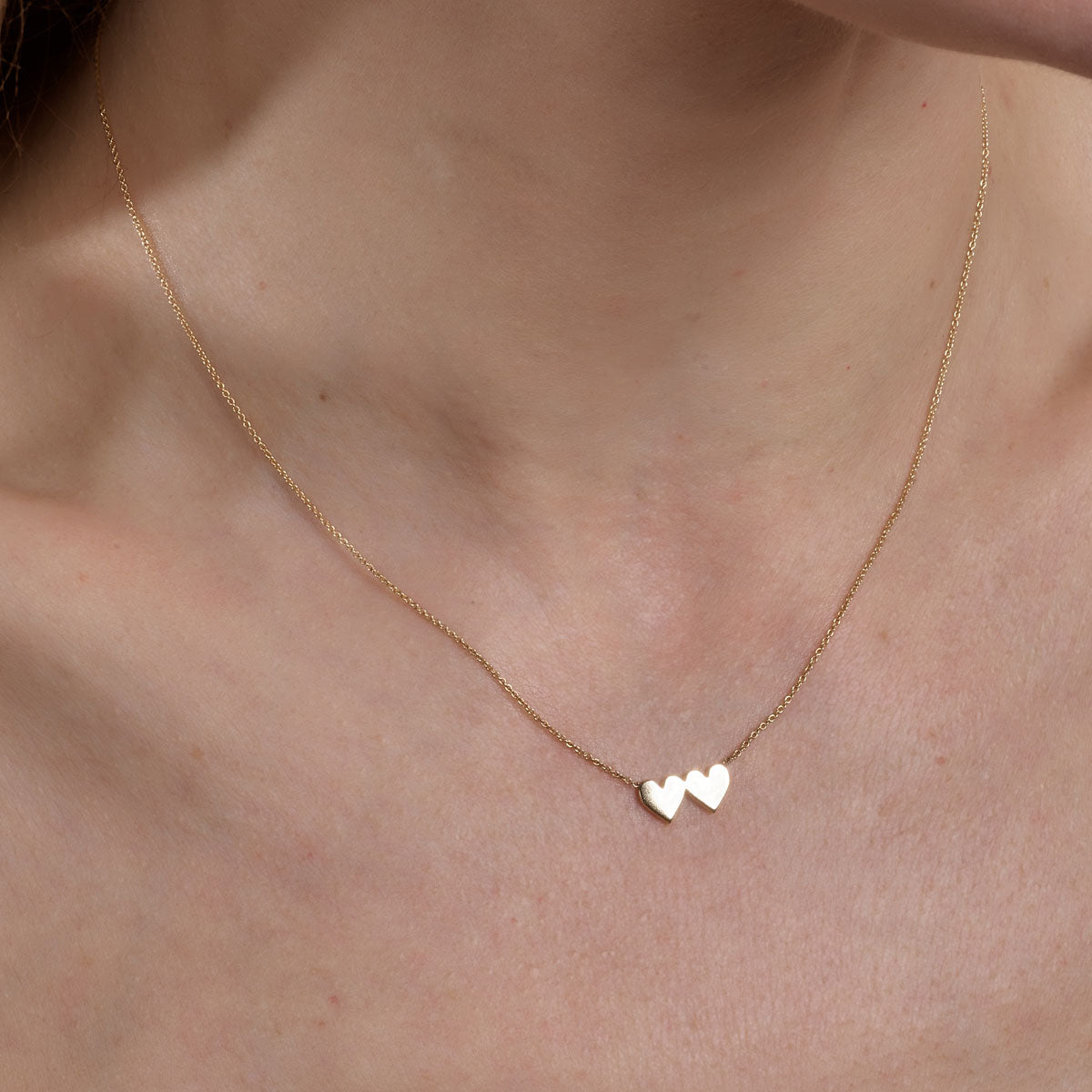 Gold double heart necklace on woman's neck – delicate layered hearts pendant by Phoenix Roze