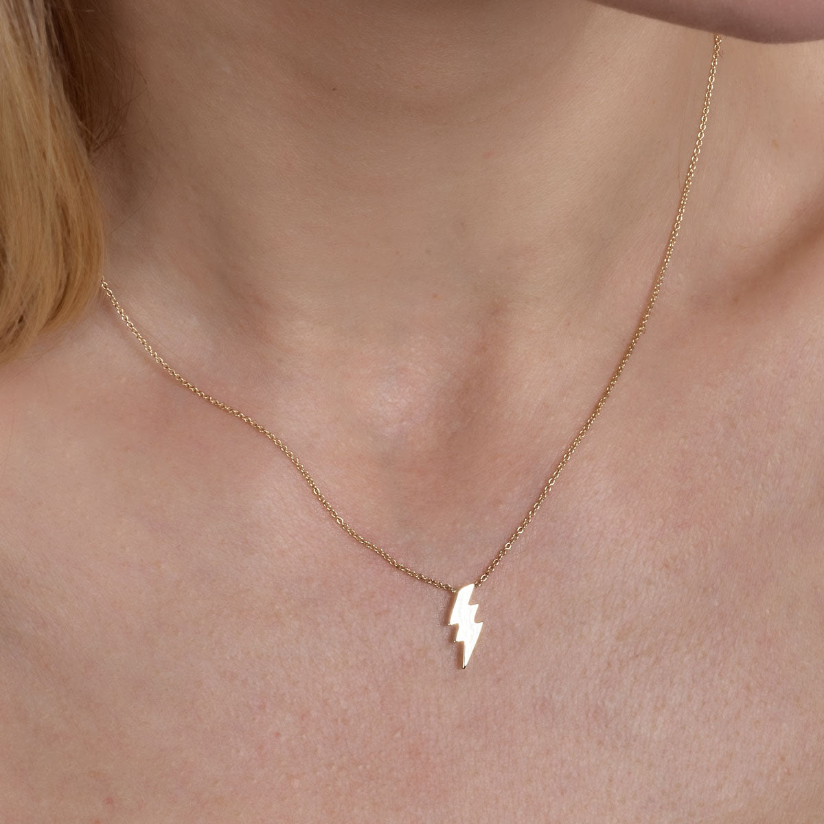 Delicate gold lightning bolt pendant necklace on woman's neck, minimalist fine jewelry by Phoenix Roze