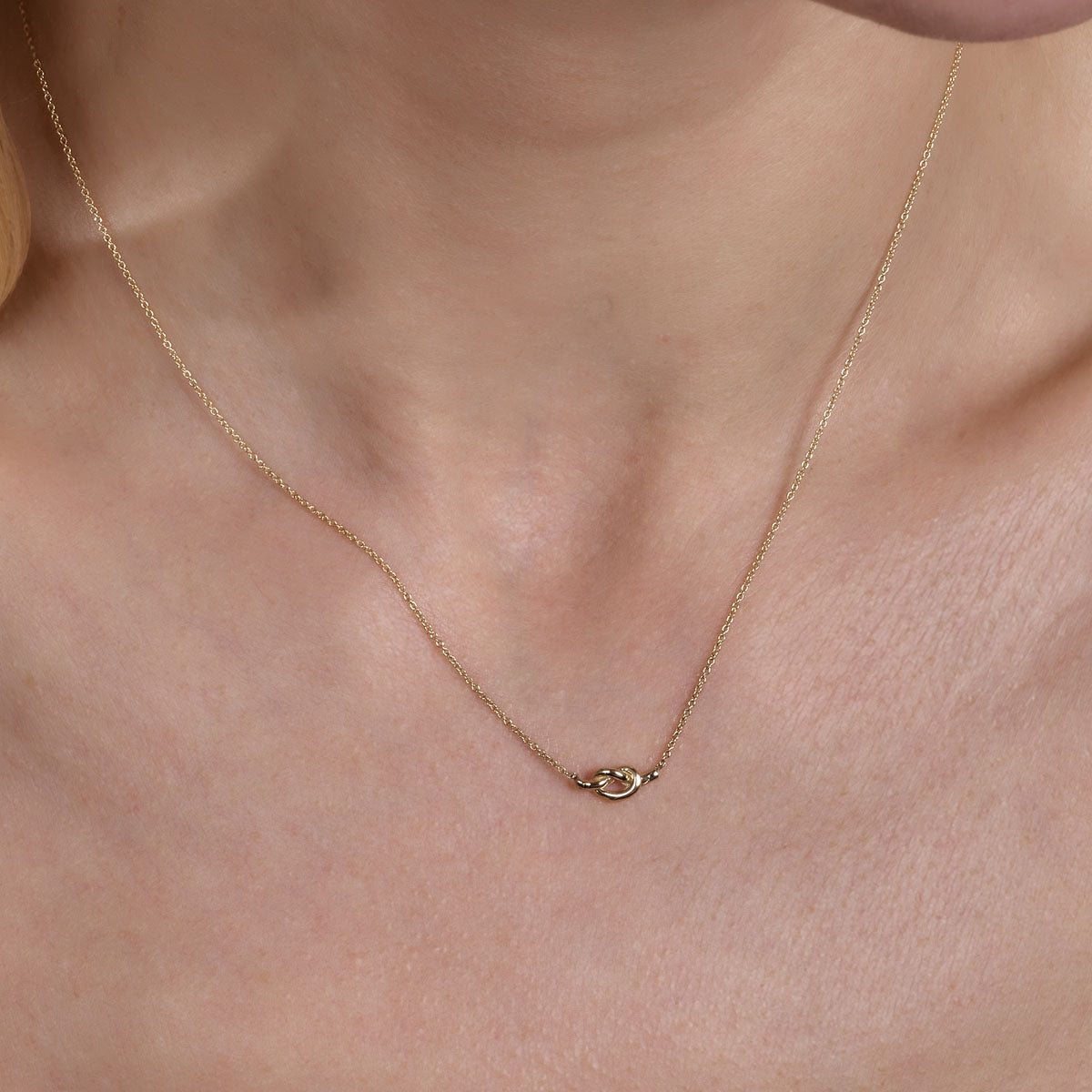 Gold love knot necklace on woman's neck, delicate and elegant Phoenix Roze jewelry