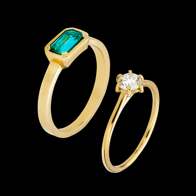 A bezel-set emerald engagement ring and a round diamond solitaire ring, both in gold