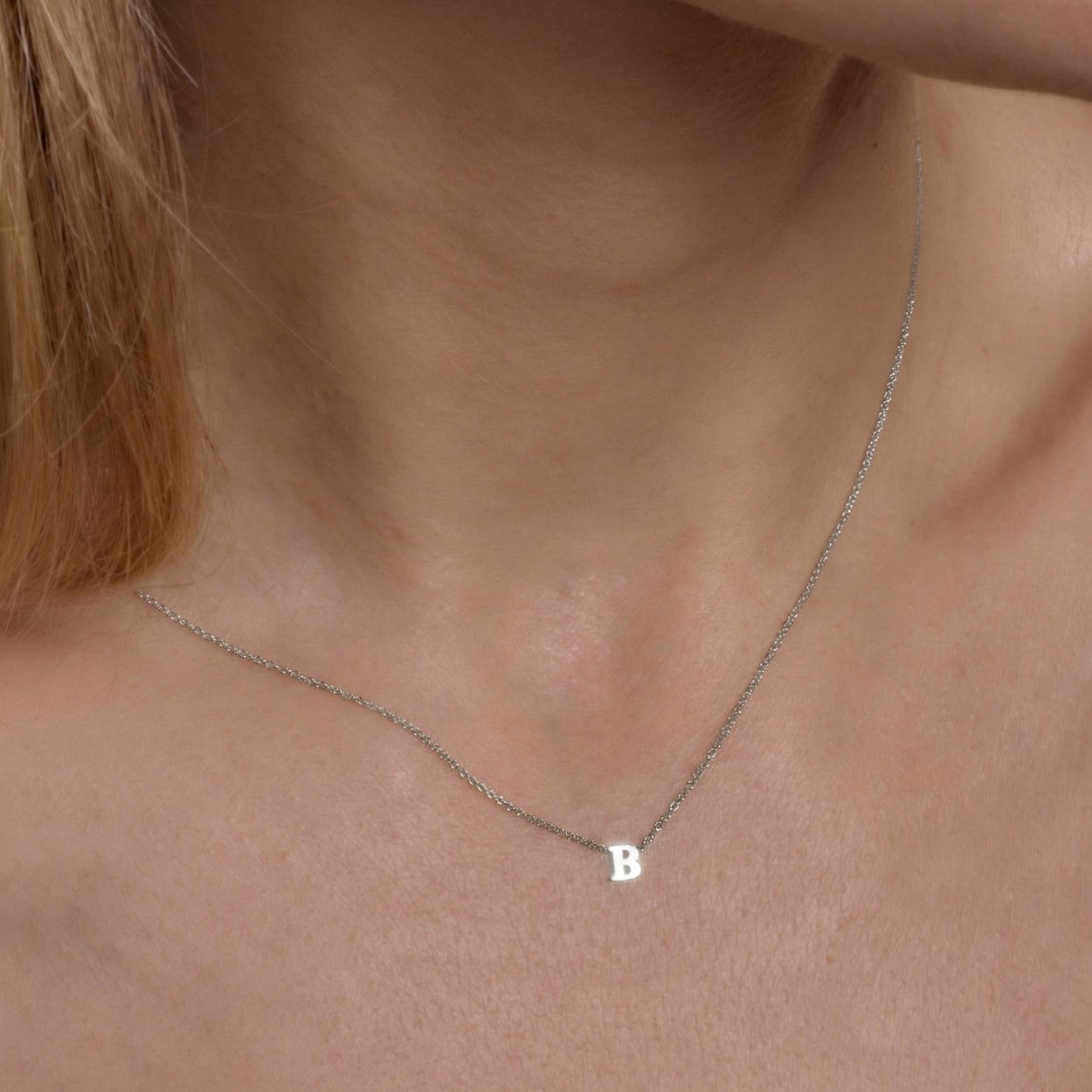 A woman wearing a delicate silver chain necklace featuring a central, single letter B pendant.