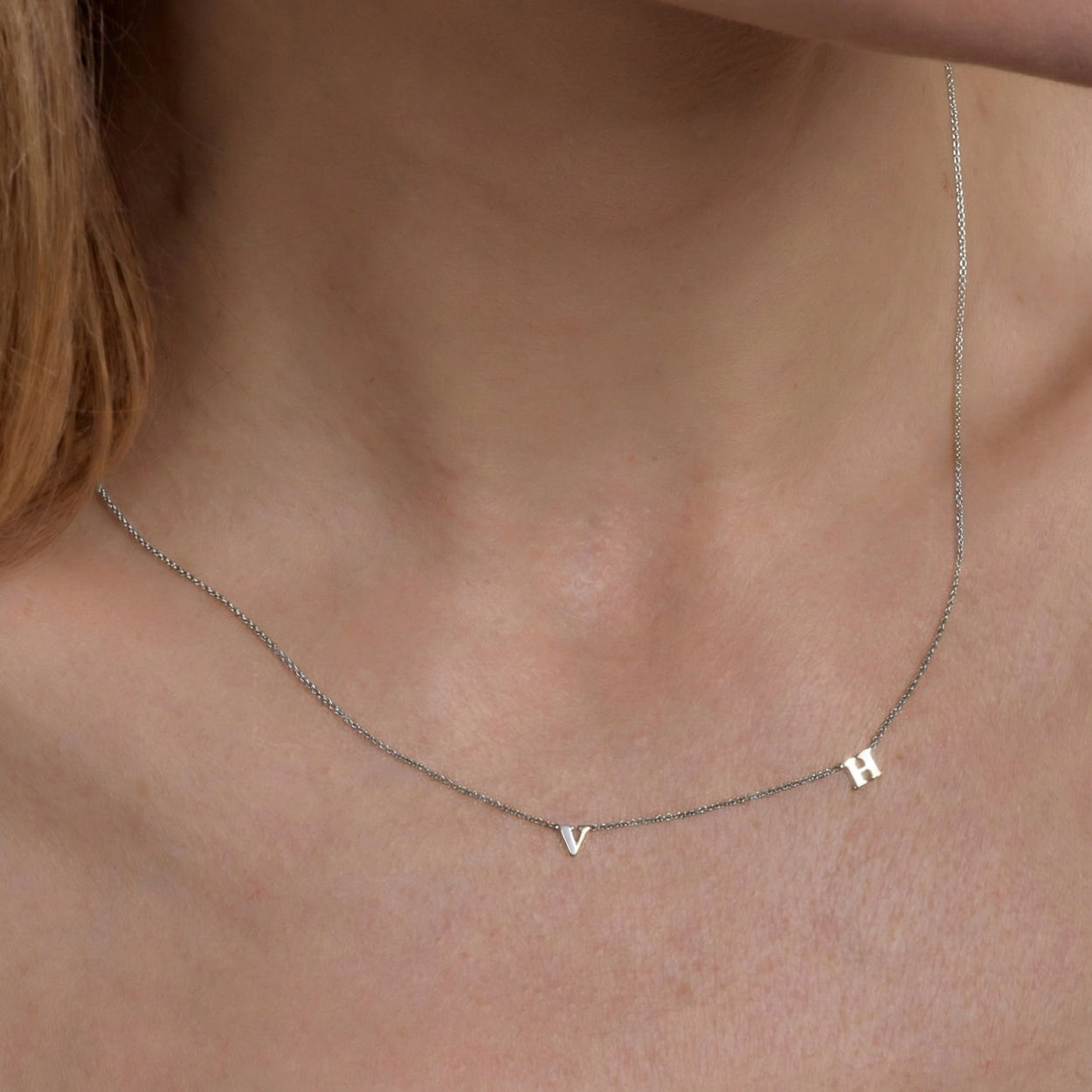A minimalist silver chain necklace featuring two spaced-out initial charms, the letters V and H.