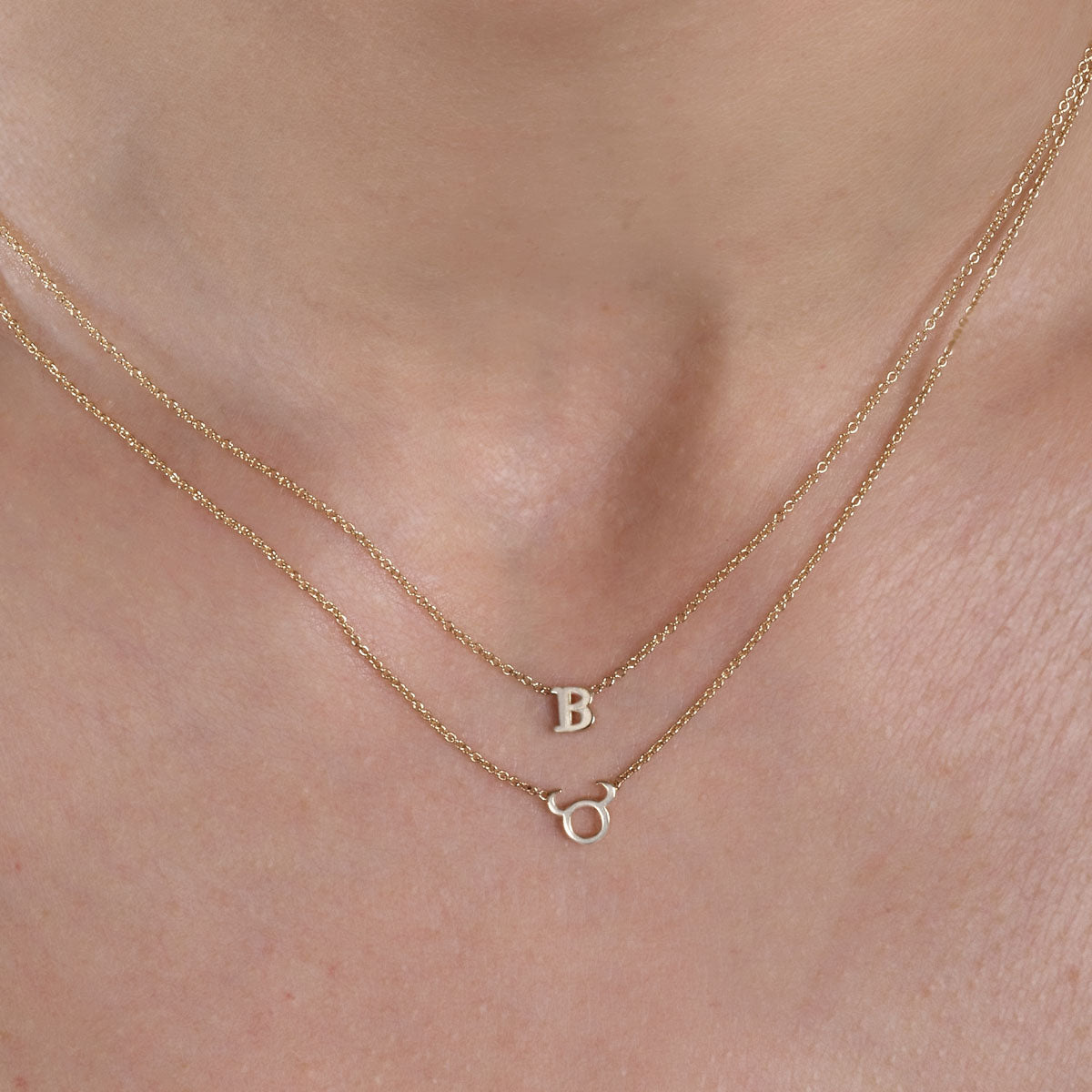 gold 1 letter initial necklace and gold taurus necklace on womans neck