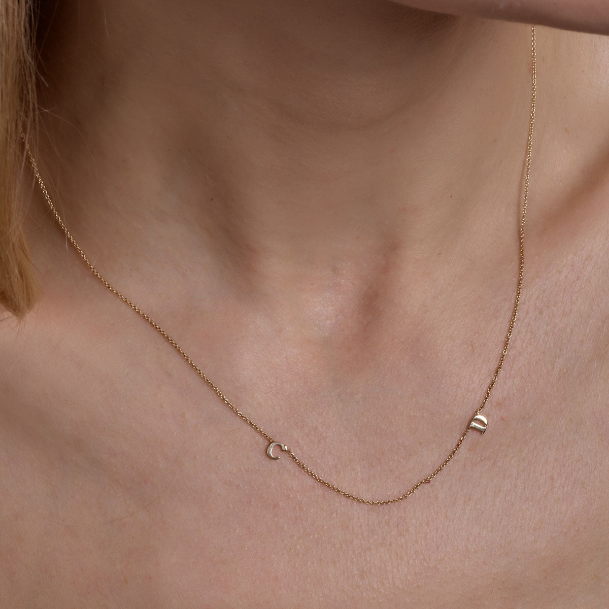 gold 2 letter initial necklace on womans neck