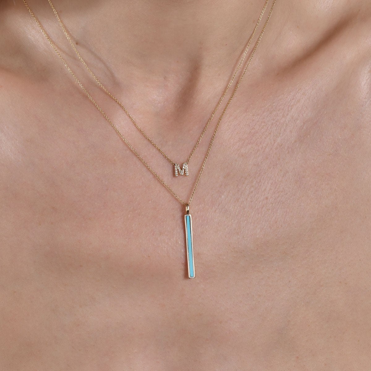 gold diamond 1 letter initial necklace and gold turquoise long bar necklace on models neck