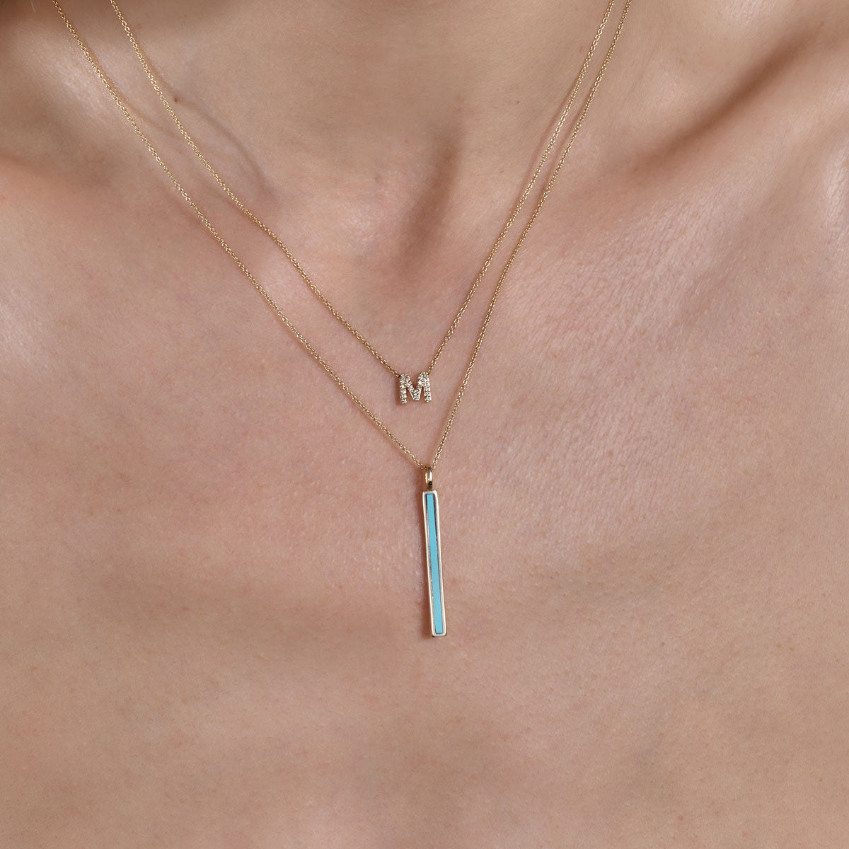 Model wearing gold diamond initial and turquoise bar necklaces, showcasing sophistication & style.