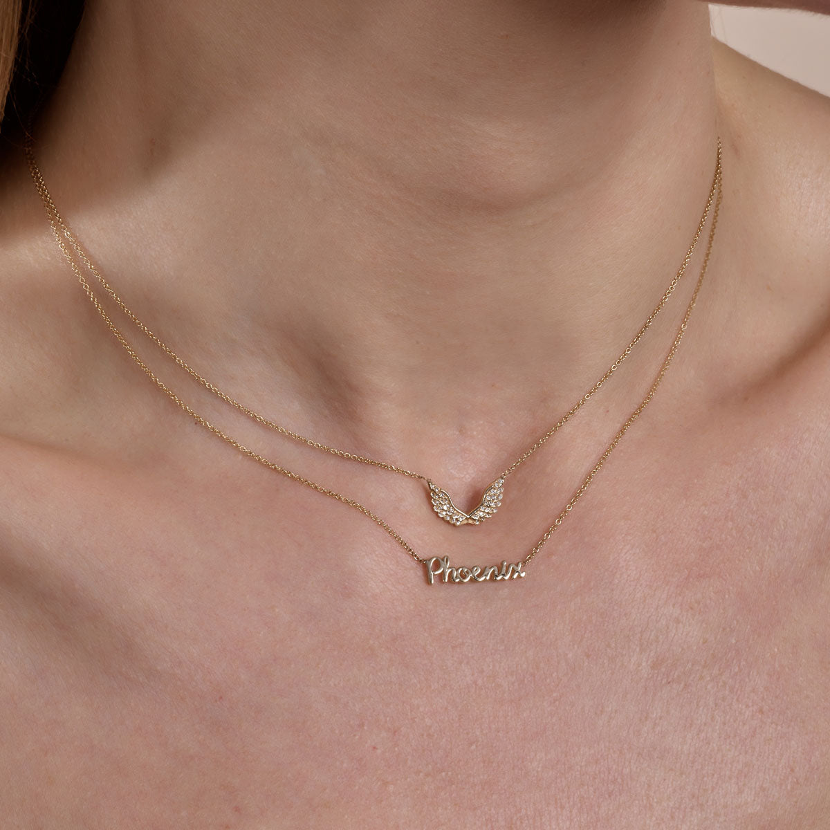 gold diamond angel wings necklace and gold cursive phoenix necklace on neck