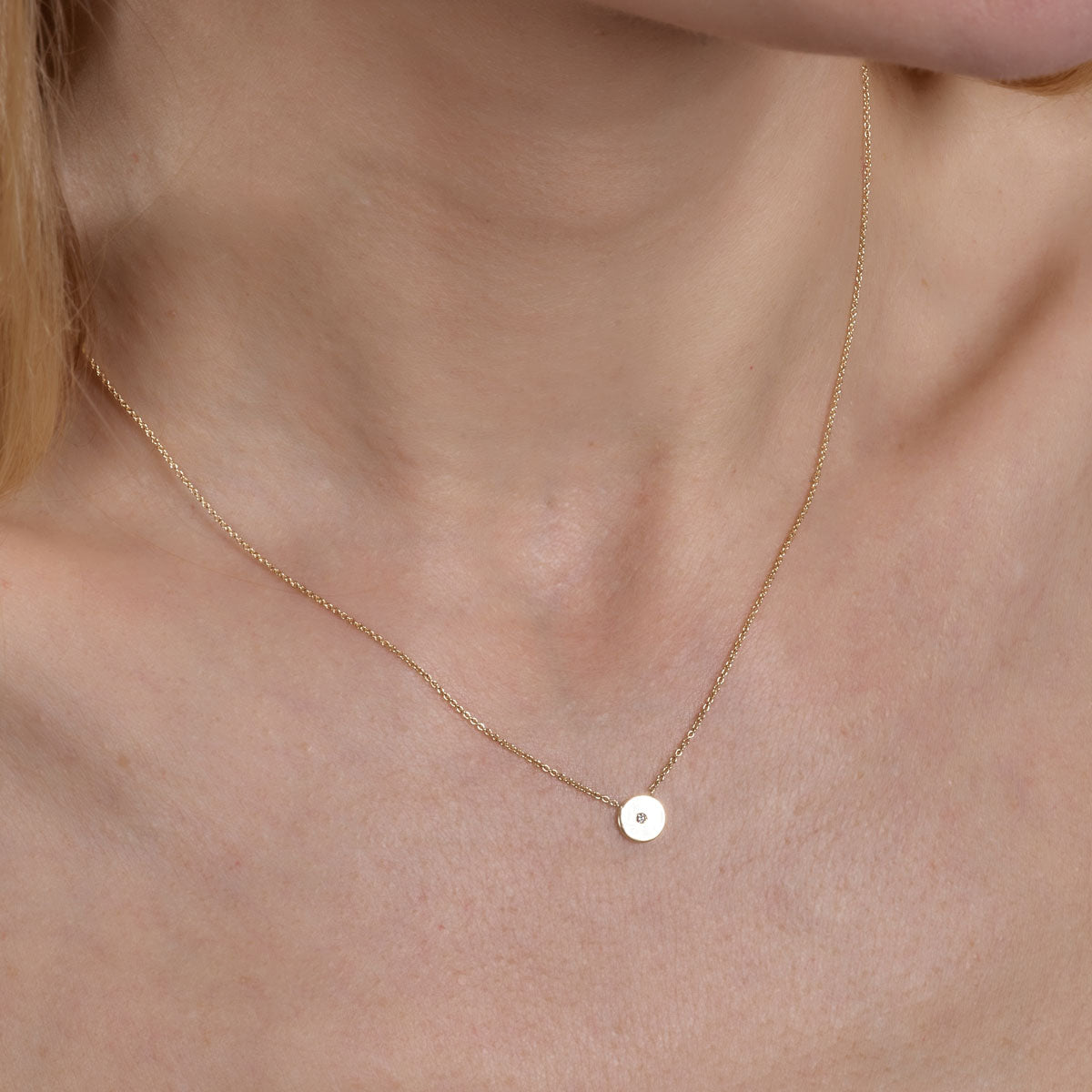 gold diamond round necklace on womans neck