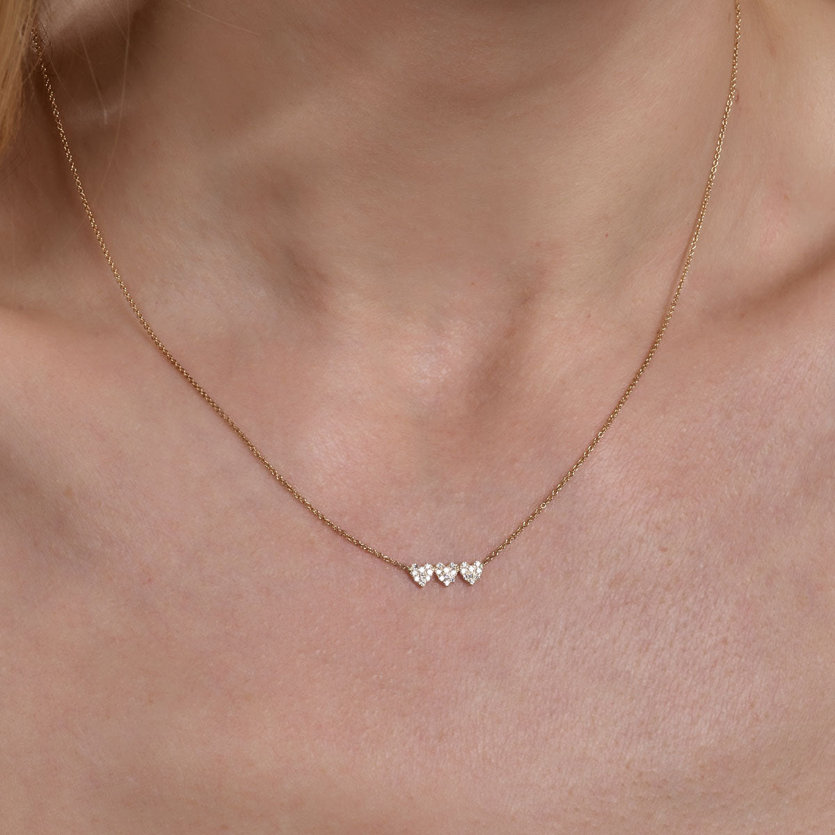 gold diamond triple heart necklace on womans neck