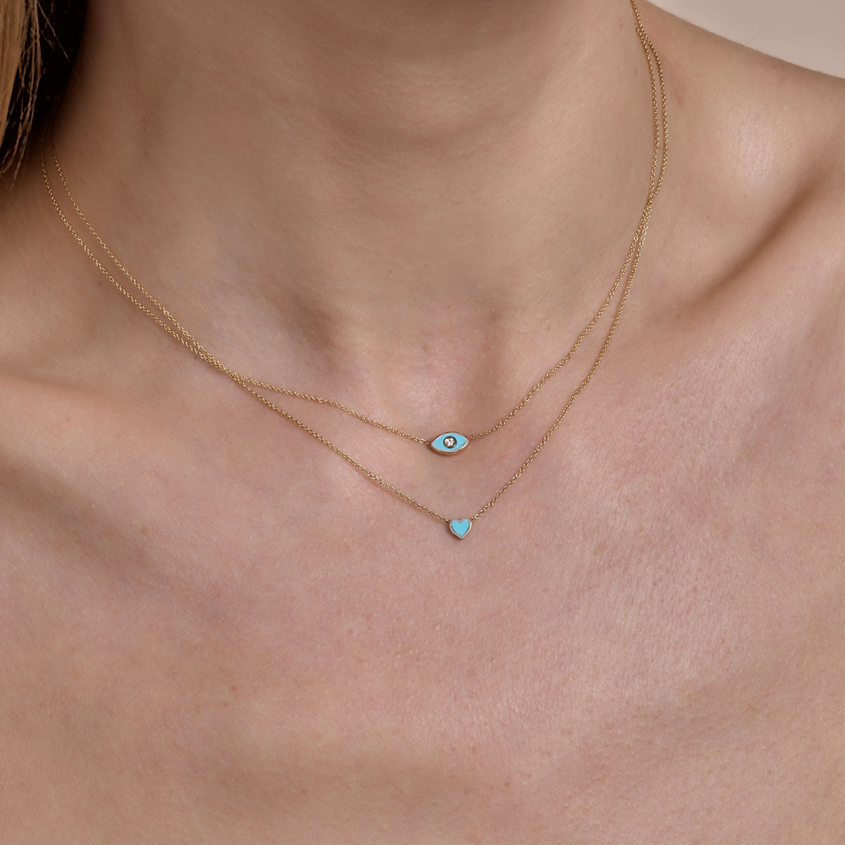 gold turquoise evil eye necklace and gold turquoise heart necklace on models neck