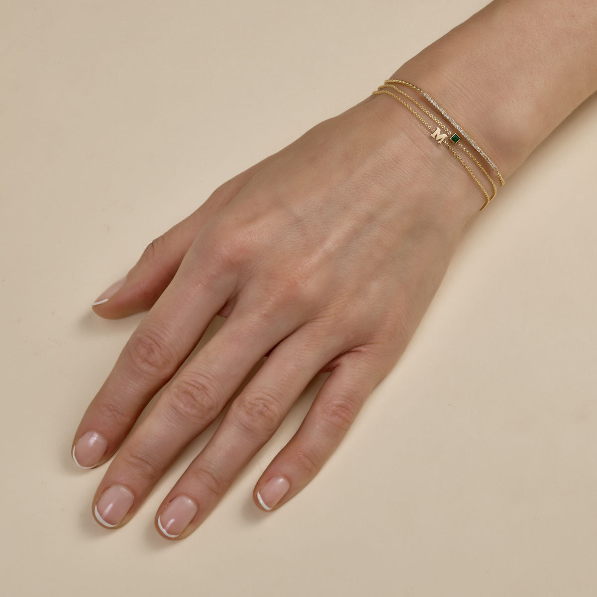 multiple gold diamond and initial bracelets stacked on womans hand